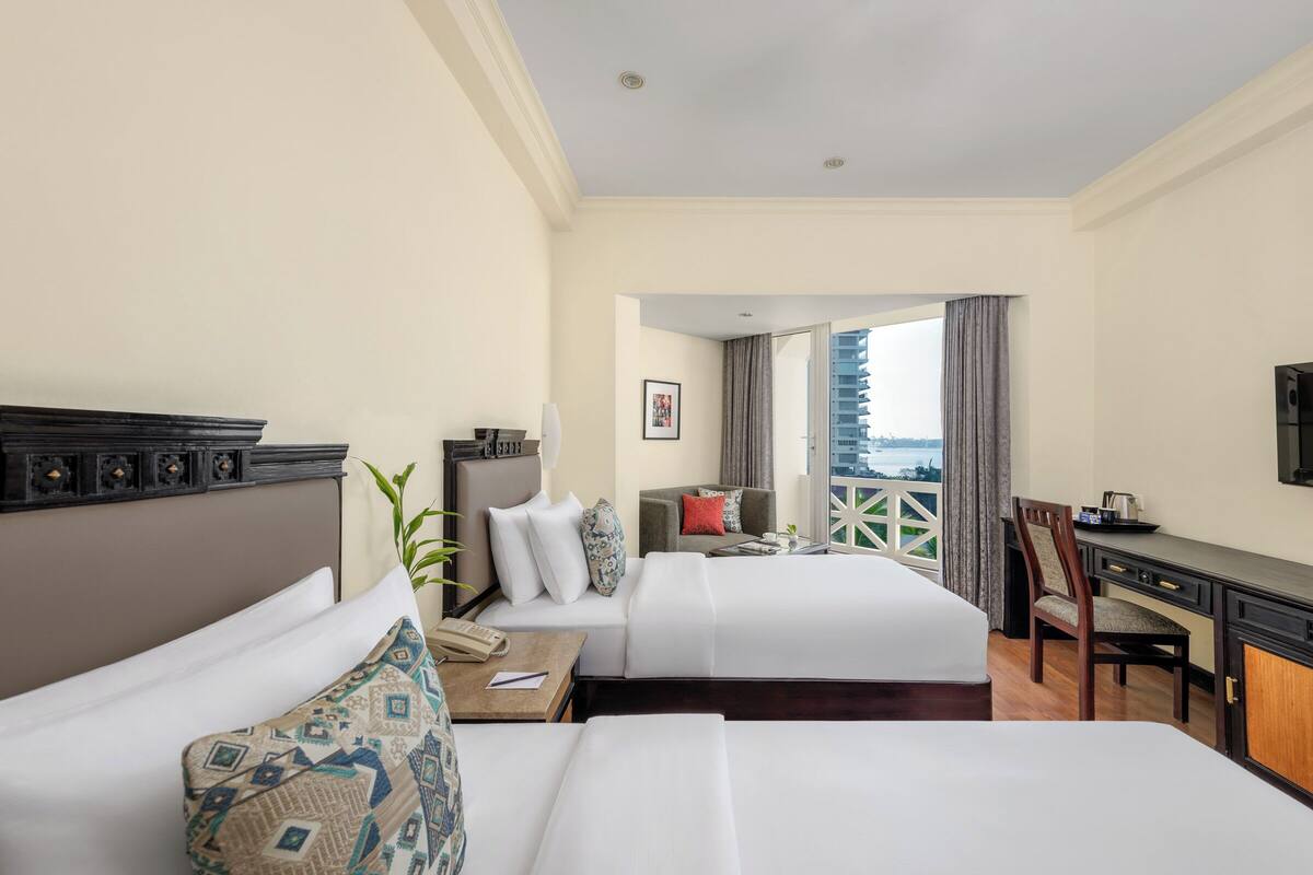 A hotel room with two beds, a desk, a chair, and a view of the city.