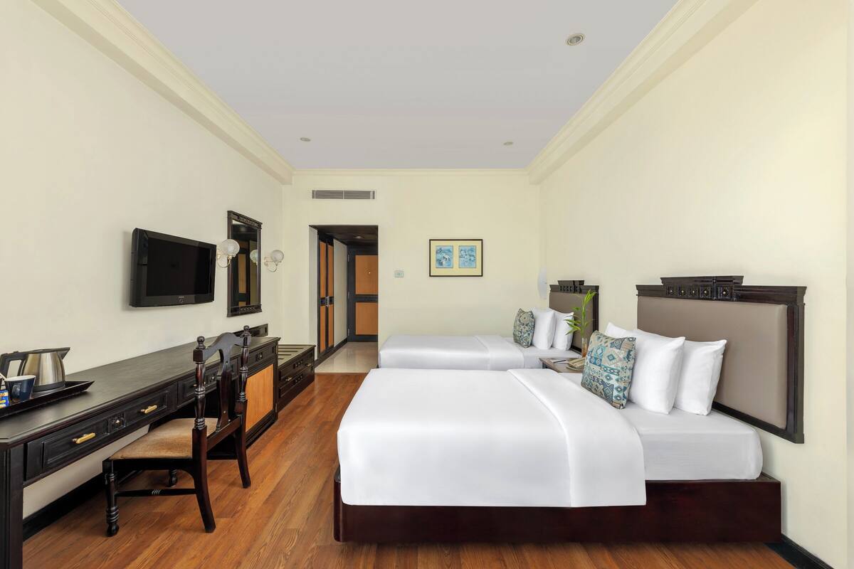 A hotel room with two beds, a desk, a TV, and a door leading to a bathroom.