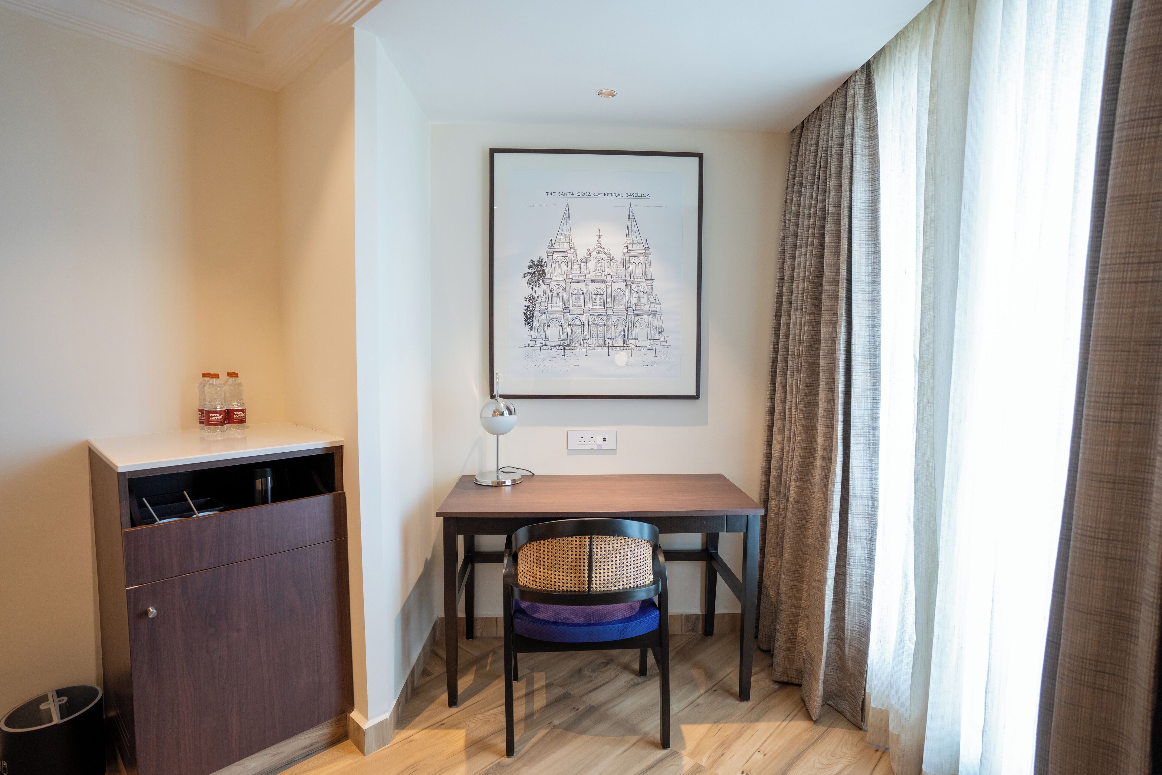 A room with a desk, chair, and a framed picture of a cathedral.