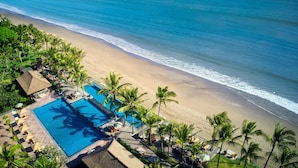 An aerial view of a beach resort with a swimming pool, palm trees, and a beach.