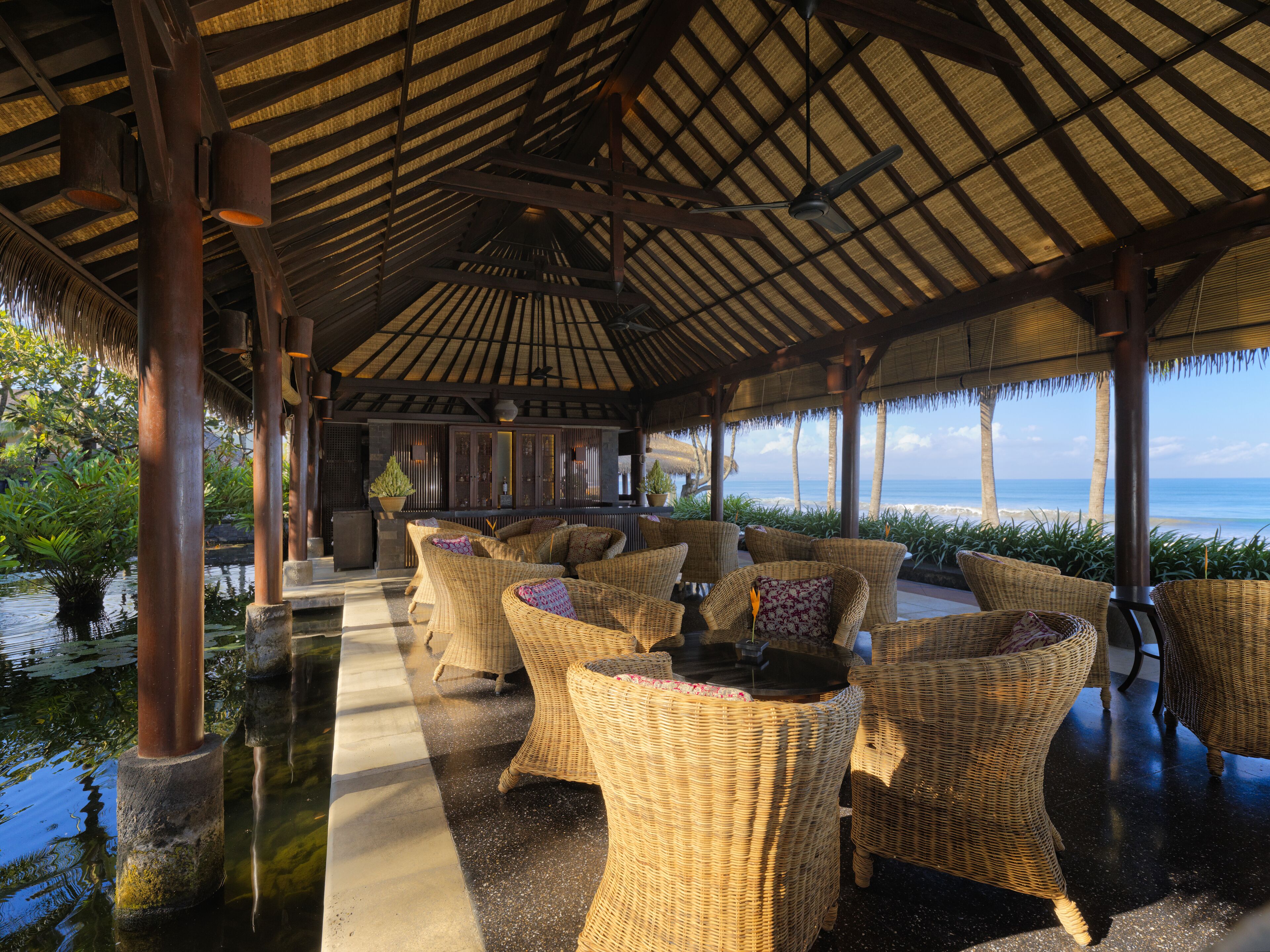 A covered outdoor seating area with wicker furniture, a water feature, and a view of the ocean.