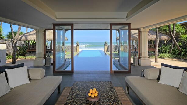 A luxurious room with a glass door leading to a private infinity pool overlooking the ocean.