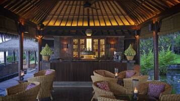 A covered outdoor seating area with wicker furniture and candles, a bar with a wooden counter, and a thatched roof structure.