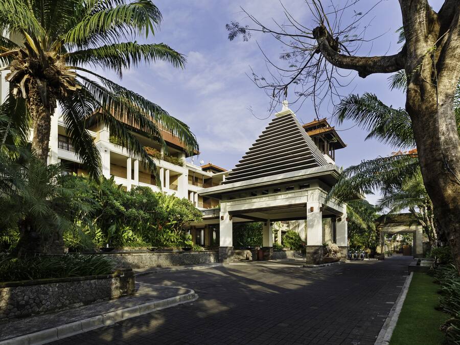 A hotel entrance with a covered walkway, palm trees, and a stone pathway.