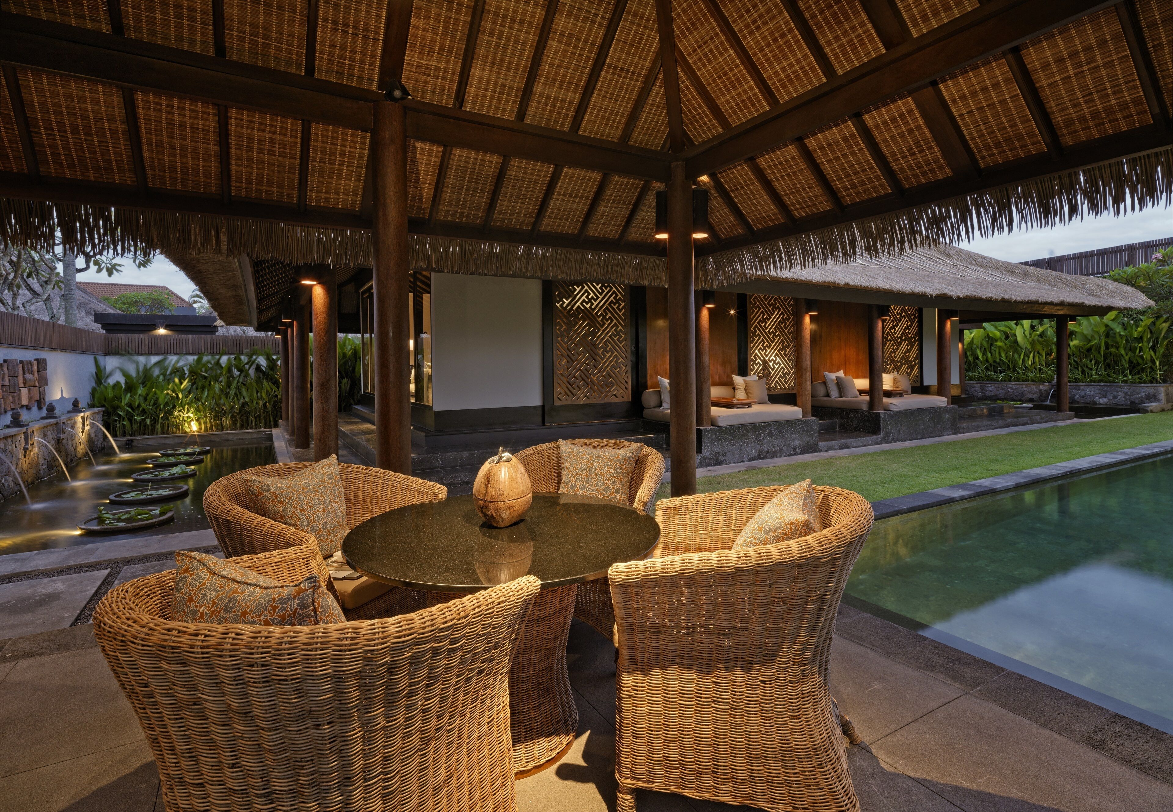 A covered outdoor seating area with wicker furniture and a pool.