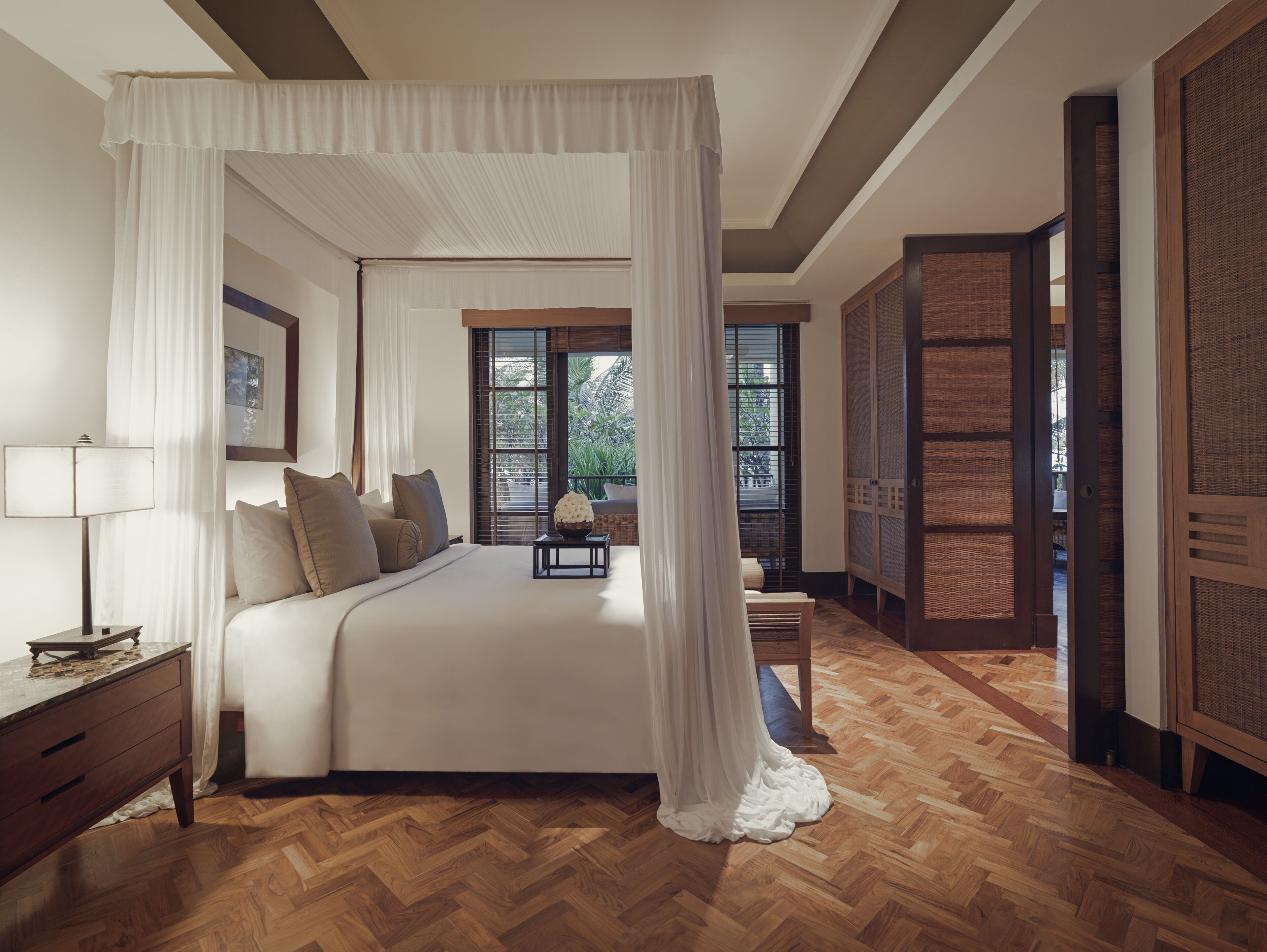 A bedroom with a four-poster bed, wooden flooring, and a view of the outdoors through a window.