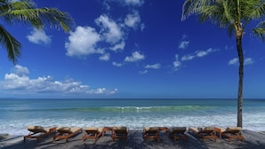 A wooden deck with lounge chairs and a bed, overlooking a beach with palm trees and the ocean. - The Legian Seminyak, Bali (Seminyak)