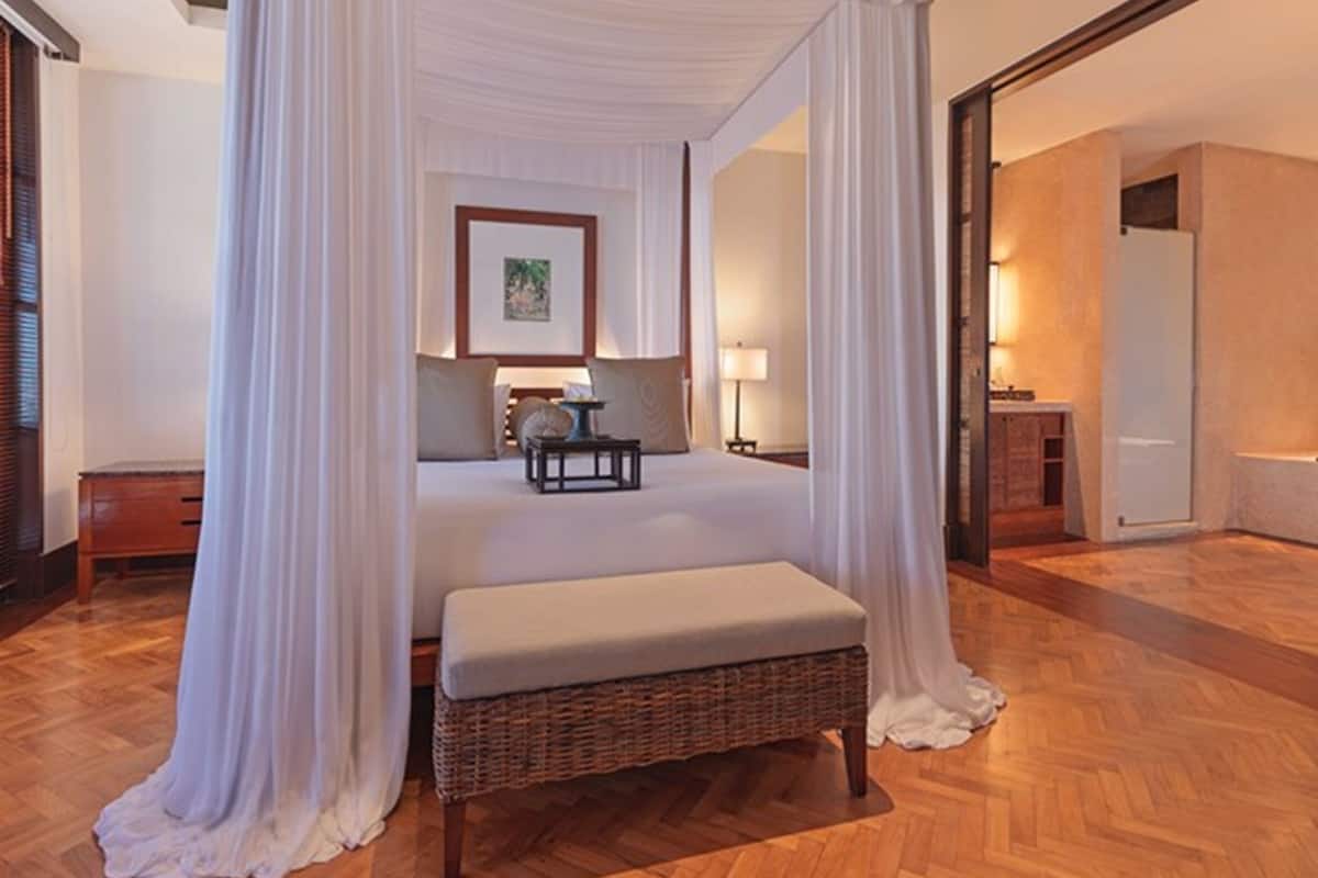 A bedroom with a four-poster canopy bed, a bedside table, a lamp, and a framed picture on the wall.