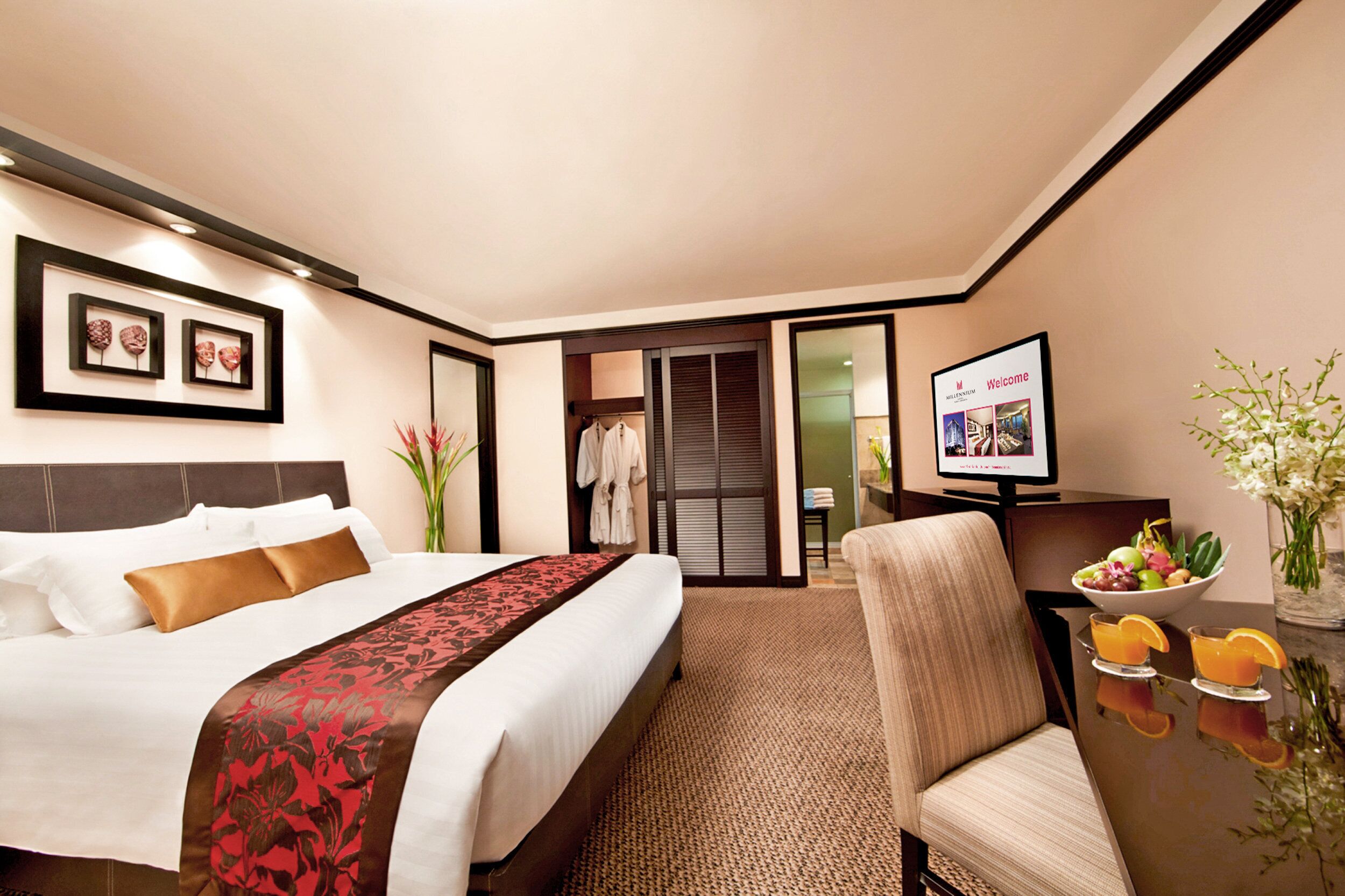 Habitación de hotel con una cama bien hecha, un televisor, una mesa de comedor con fruta y vistas al exterior.