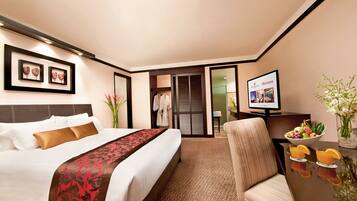 Habitación de hotel con una cama bien hecha, un televisor, una mesa de comedor con fruta y vistas al exterior.