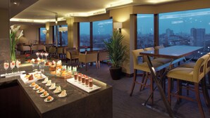 Un comedor de hotel moderno con vistas a la ciudad, una barra de postres y asientos cómodos.