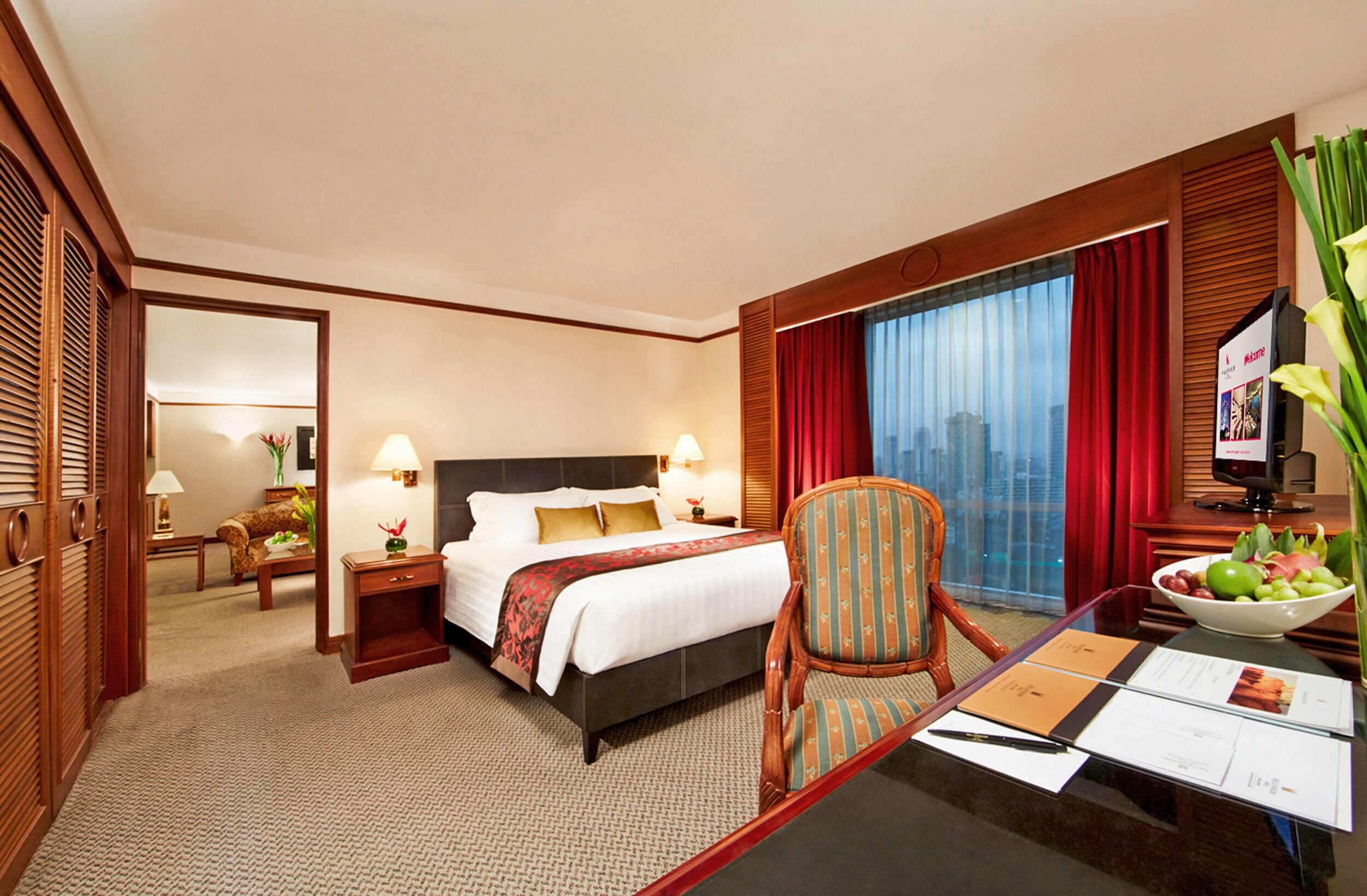 Quarto de hotel com uma cama, uma escrivaninha com cadeira, televisão e janela com cortinas.