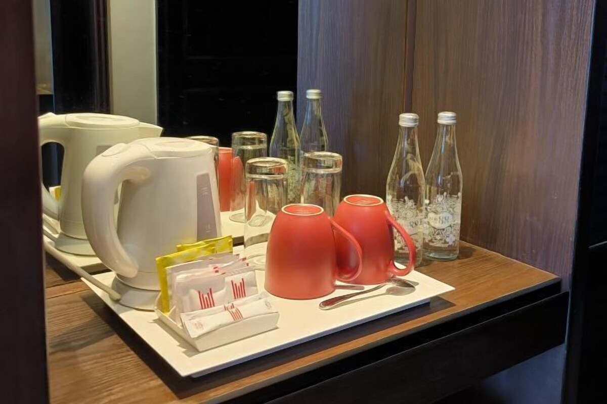 Una bandeja con una tetera, tazas, vasos y una cuchara sobre una superficie de madera.