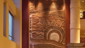 Een hal met een groot muurschilderij, een zithoek met rode en beige banken, en potplanten.