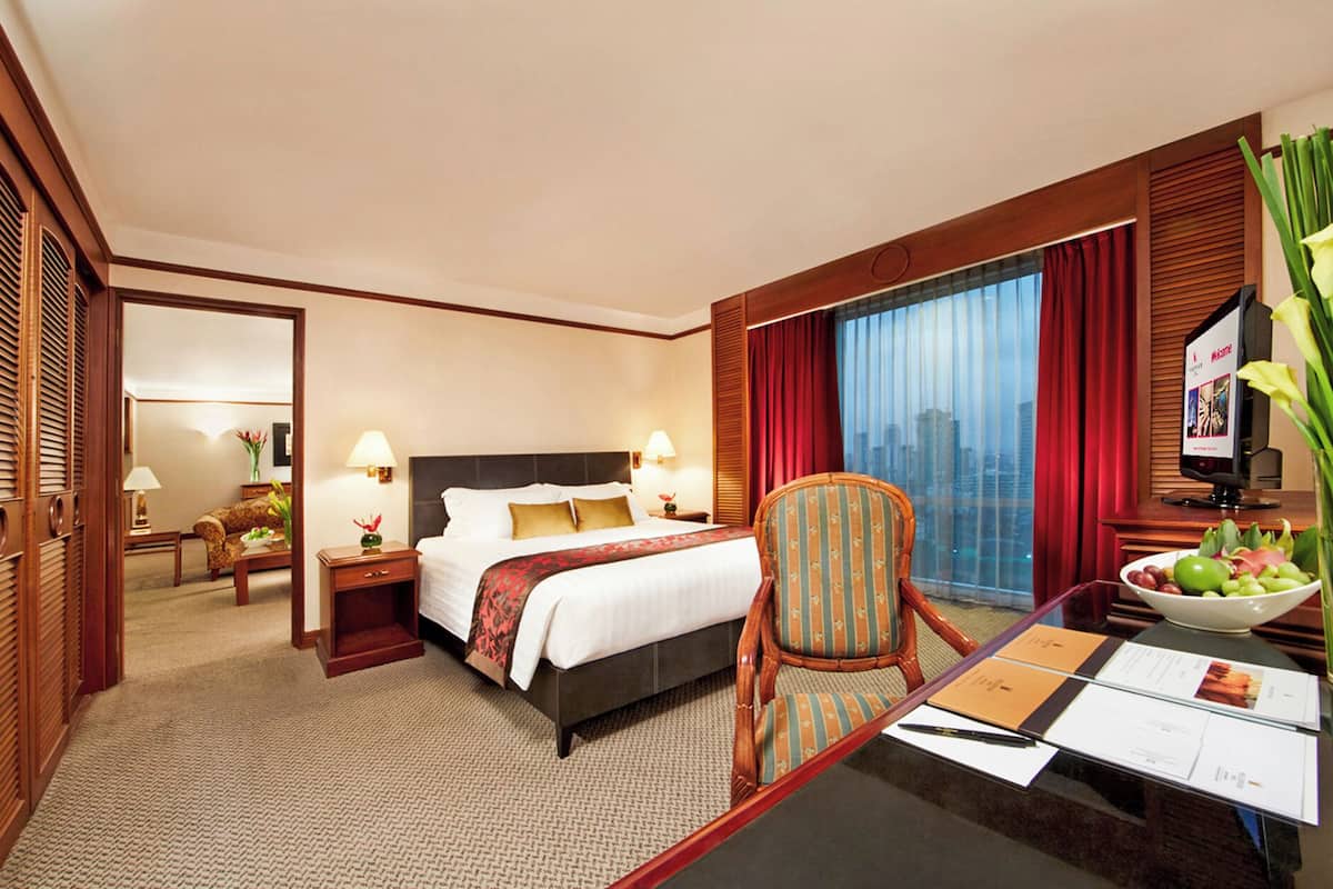 Habitación de hotel con cama, escritorio con computadora, silla, ventana con cortinas y vista a la ciudad.