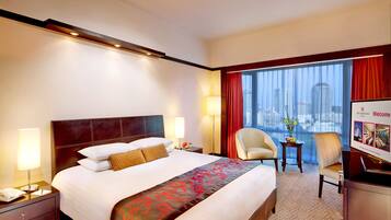 A hotel room with a large bed, a desk, a chair, a window with a city view, and a welcome sign.