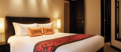 A hotel room with a large bed, two bedside lamps, a dark headboard, and a red floral bedspread.