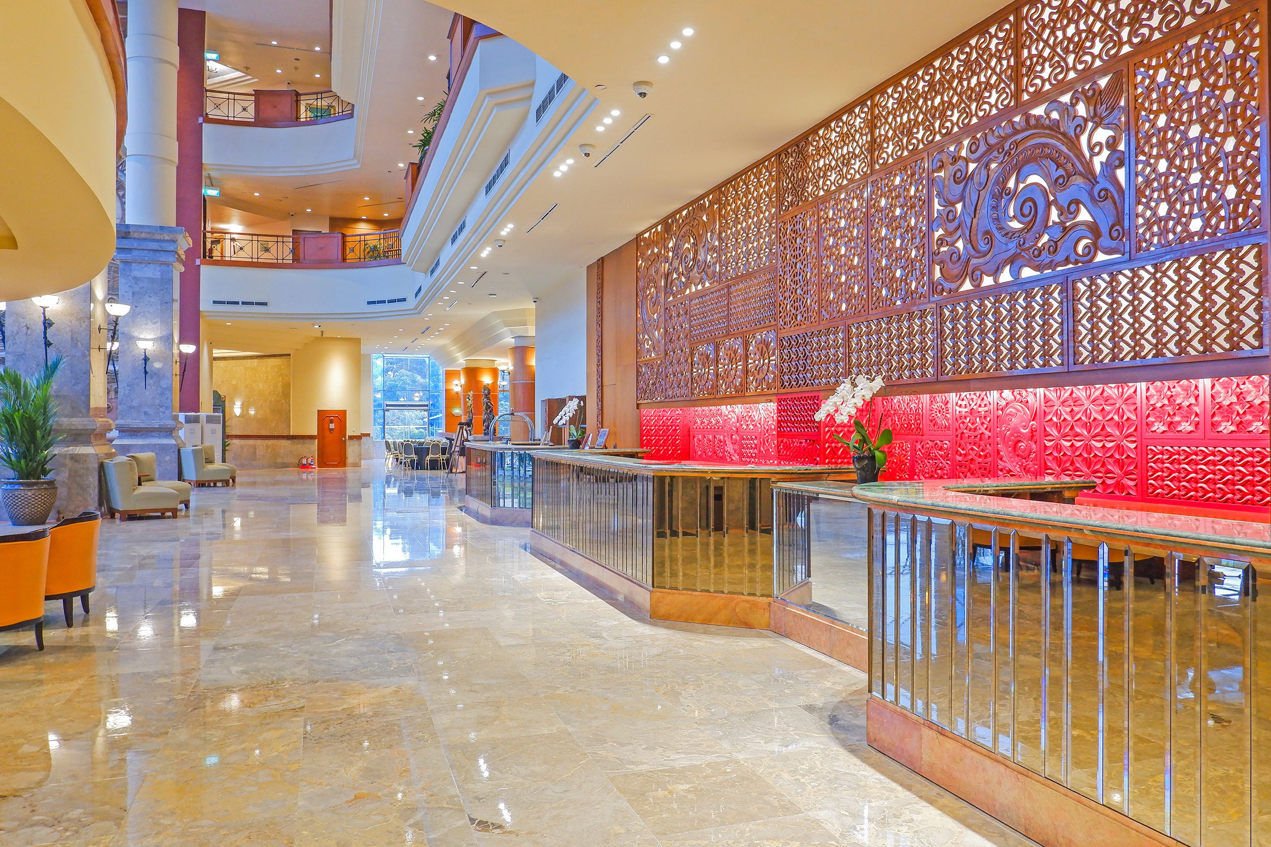 Un hall d’entrée spacieux avec un plafond haut, un comptoir d’accueil et un mur décoratif orné de motifs complexes.