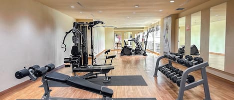 Et fitnessrum med træningsudstyr, trægulve og store vinduer.