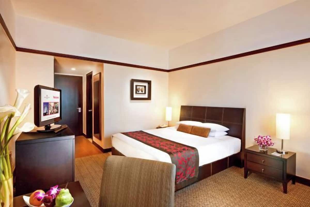 Una habitación de hotel con cama, mesitas de noche, un escritorio con computadora, una silla y televisión.