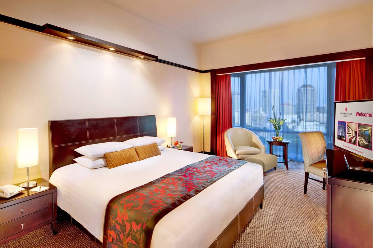 Una habitación de hotel con una cama grande, un escritorio, una silla, una lámpara de escritorio, una mesita de noche y una ventana con vistas a la ciudad.