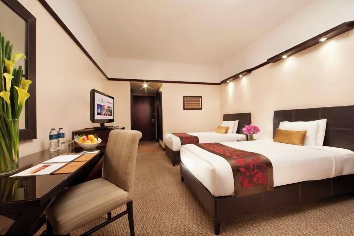 Habitación de hotel con dos camas, un escritorio con silla, un espejo y un florero con flores.