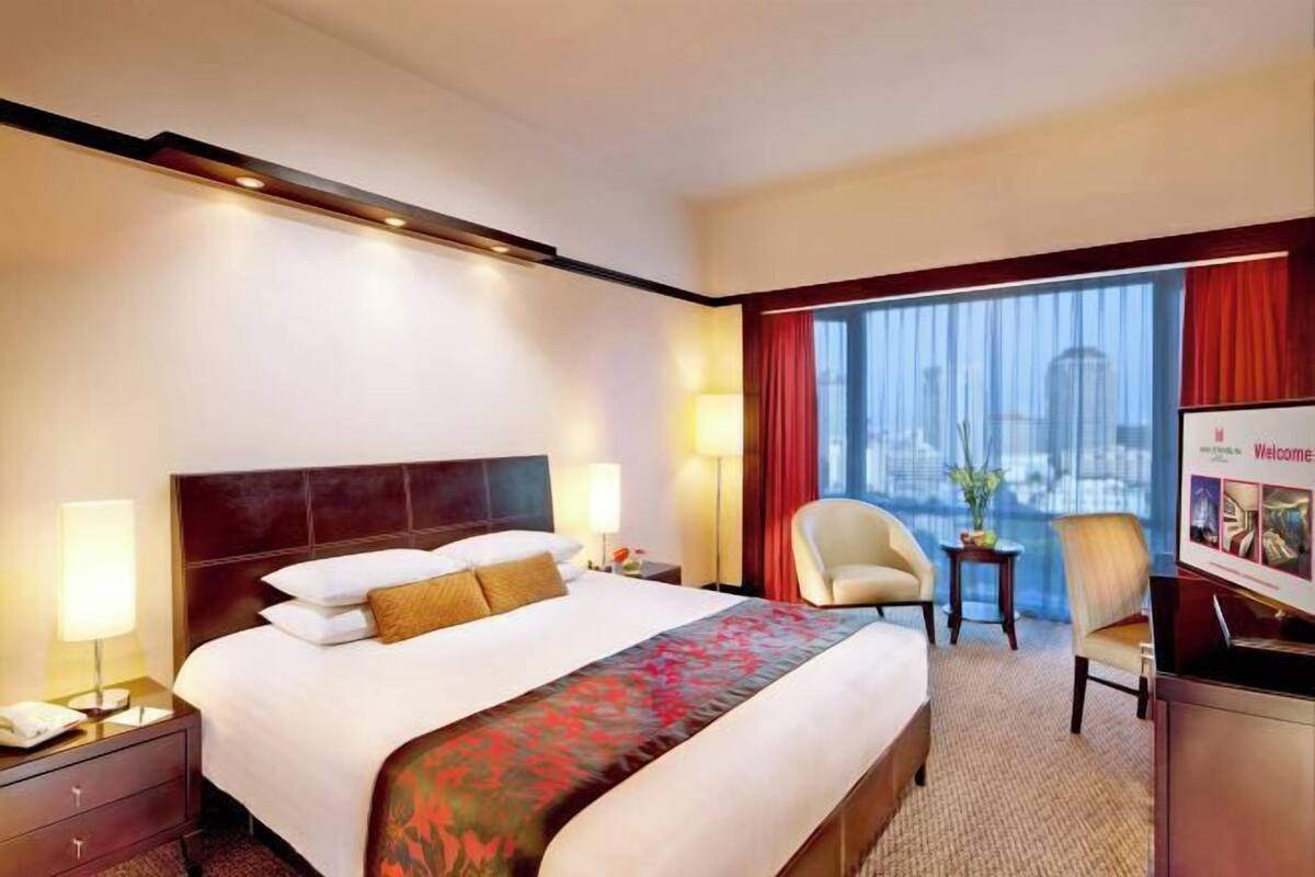 Habitación de hotel con una cama grande, un escritorio, una silla, un televisor y una ventana con vista a la ciudad.