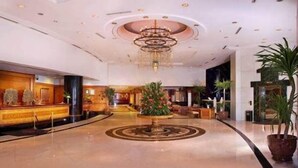 Un vestíbulo amplio con una fuente central, una recepción y un candelabro moderno.