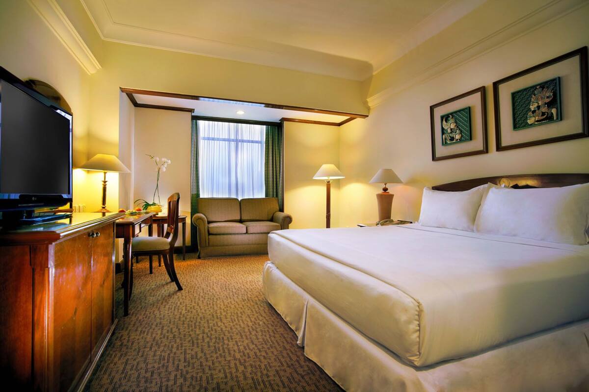 A hotel room with a large bed, a desk with a chair, a television, and two lamps.