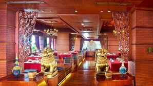 Un restaurante con elaboradas esculturas de madera, mesas rojas y estatuas doradas de leones.