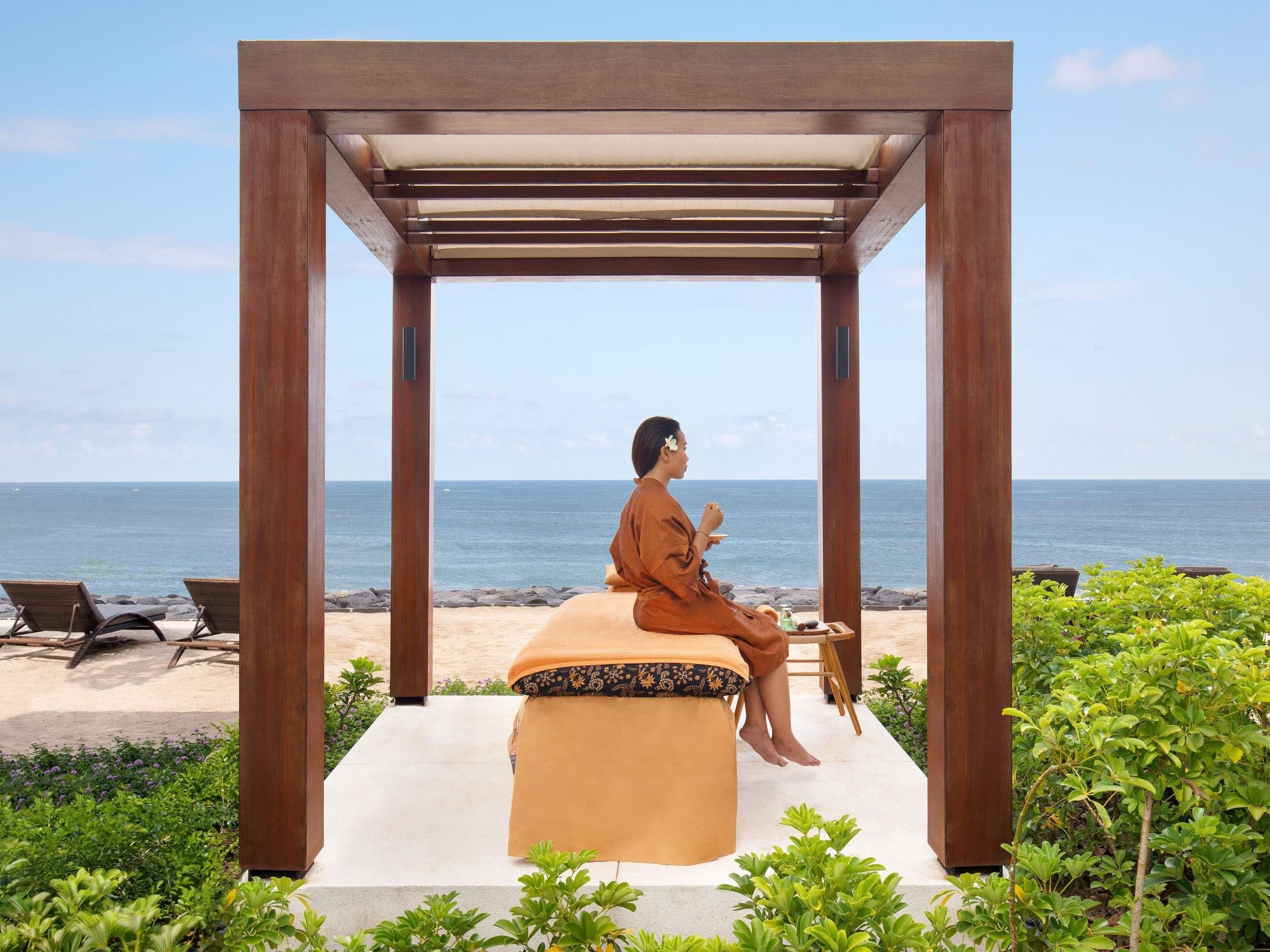 Eine Holz-Pergola mit gepolstertem Sitzplatz mit Blick auf einen Strand.