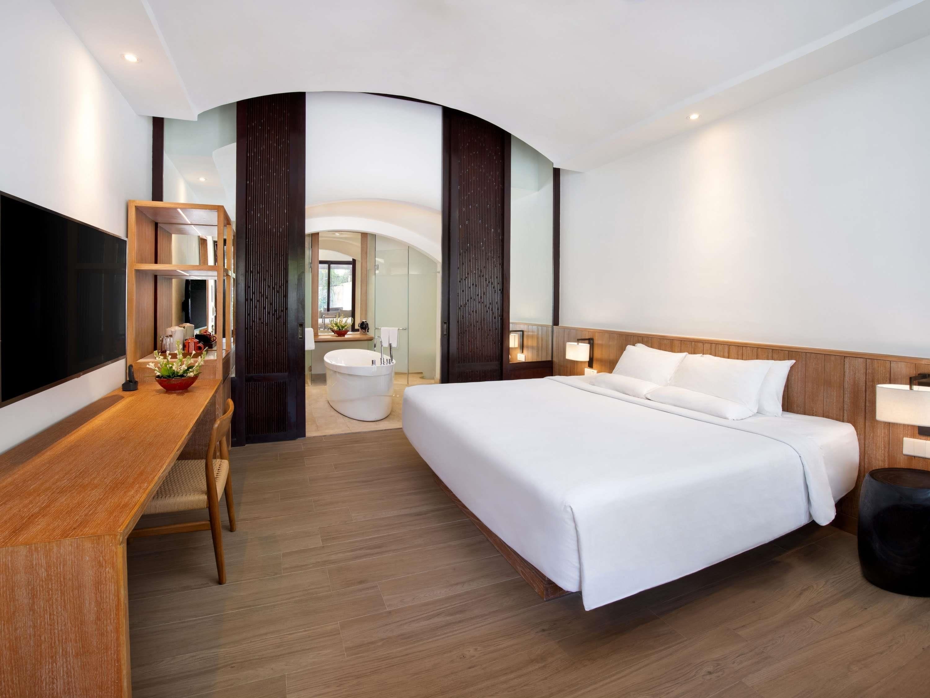 Habitación de hotel moderna con una cama grande, un escritorio con silla, televisión de pantalla plana y baño con bañera y lavamanos.