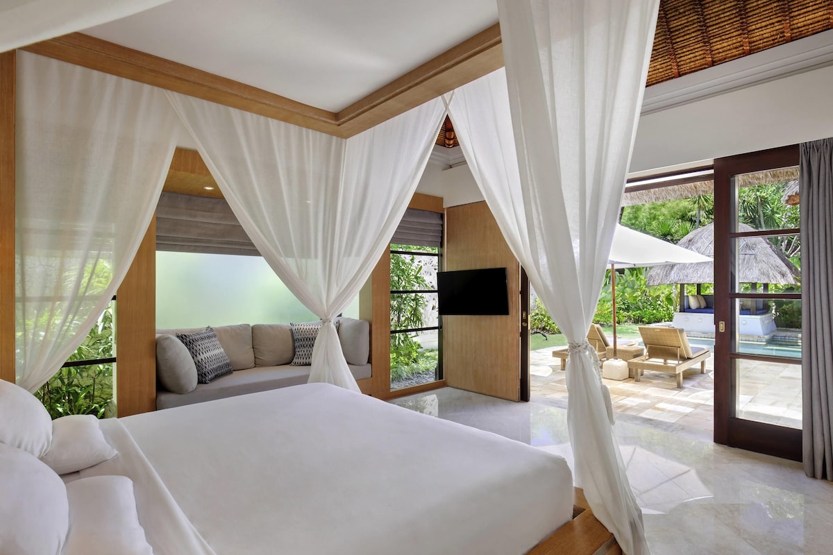 A bedroom with a bed, a TV, and a view of an outdoor pool area.