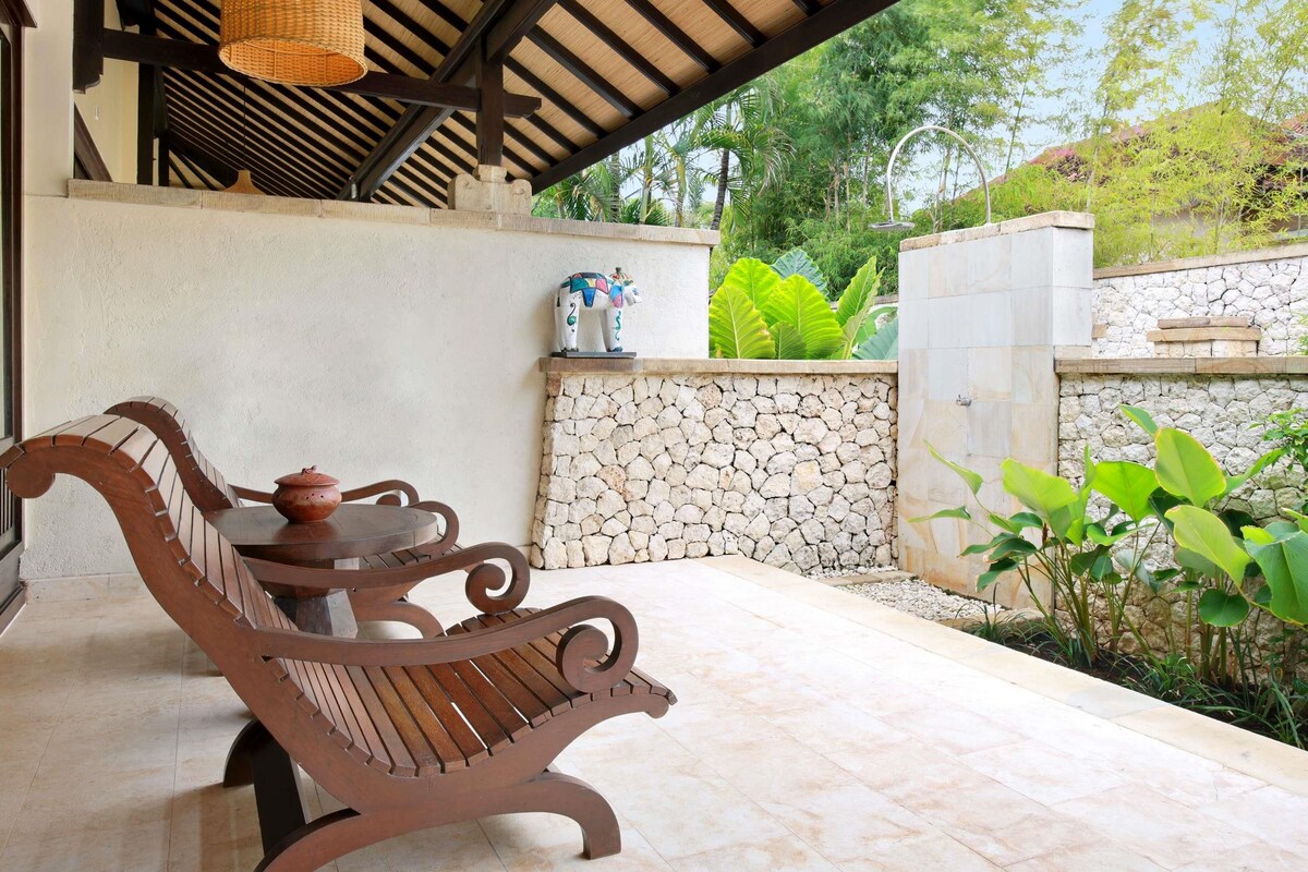 A covered patio area with a wooden bench, a table, and a stone wall.