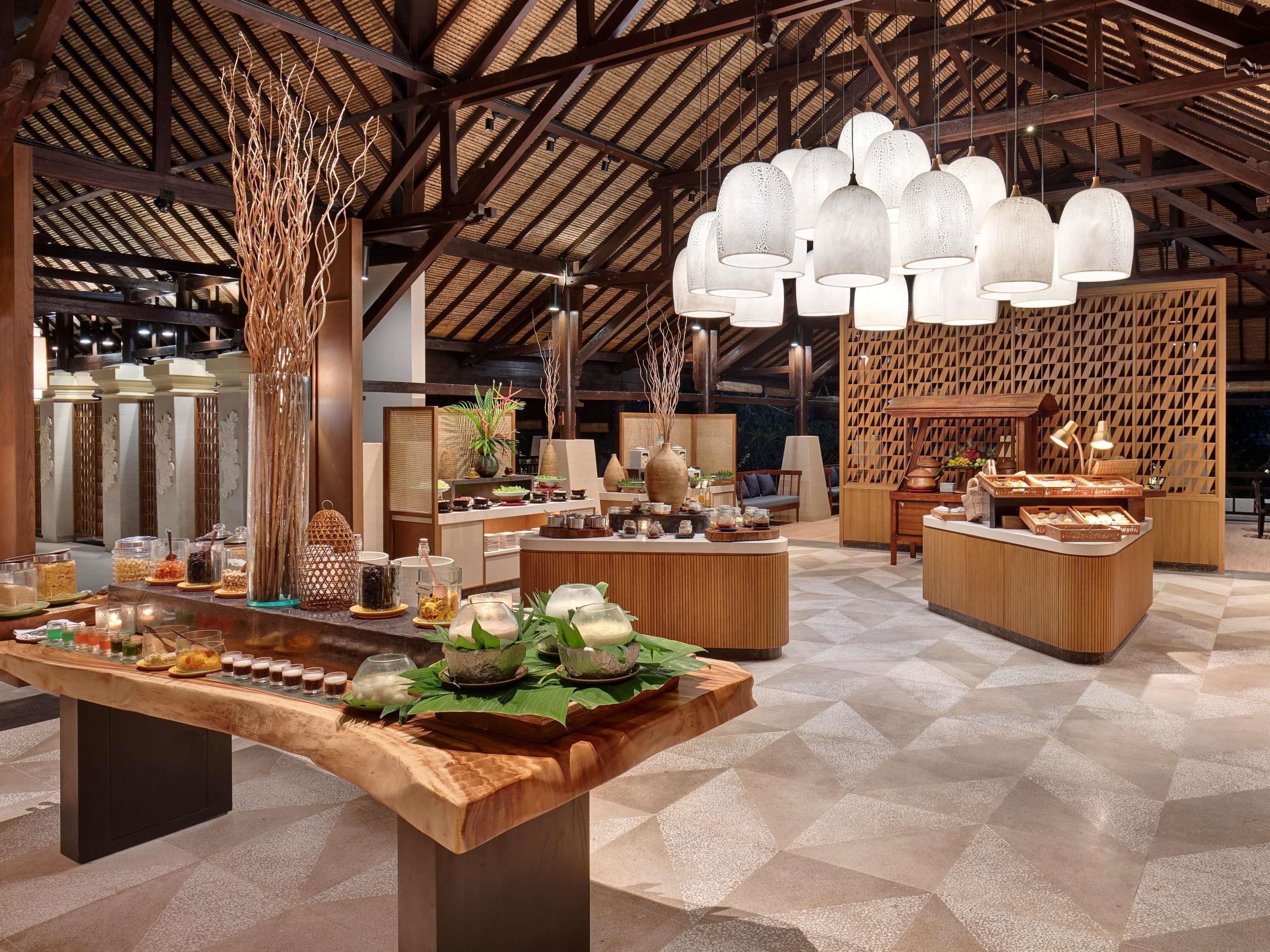 A spacious hotel lobby with a high ceiling, wooden beams, and a central serving area with food and drinks.