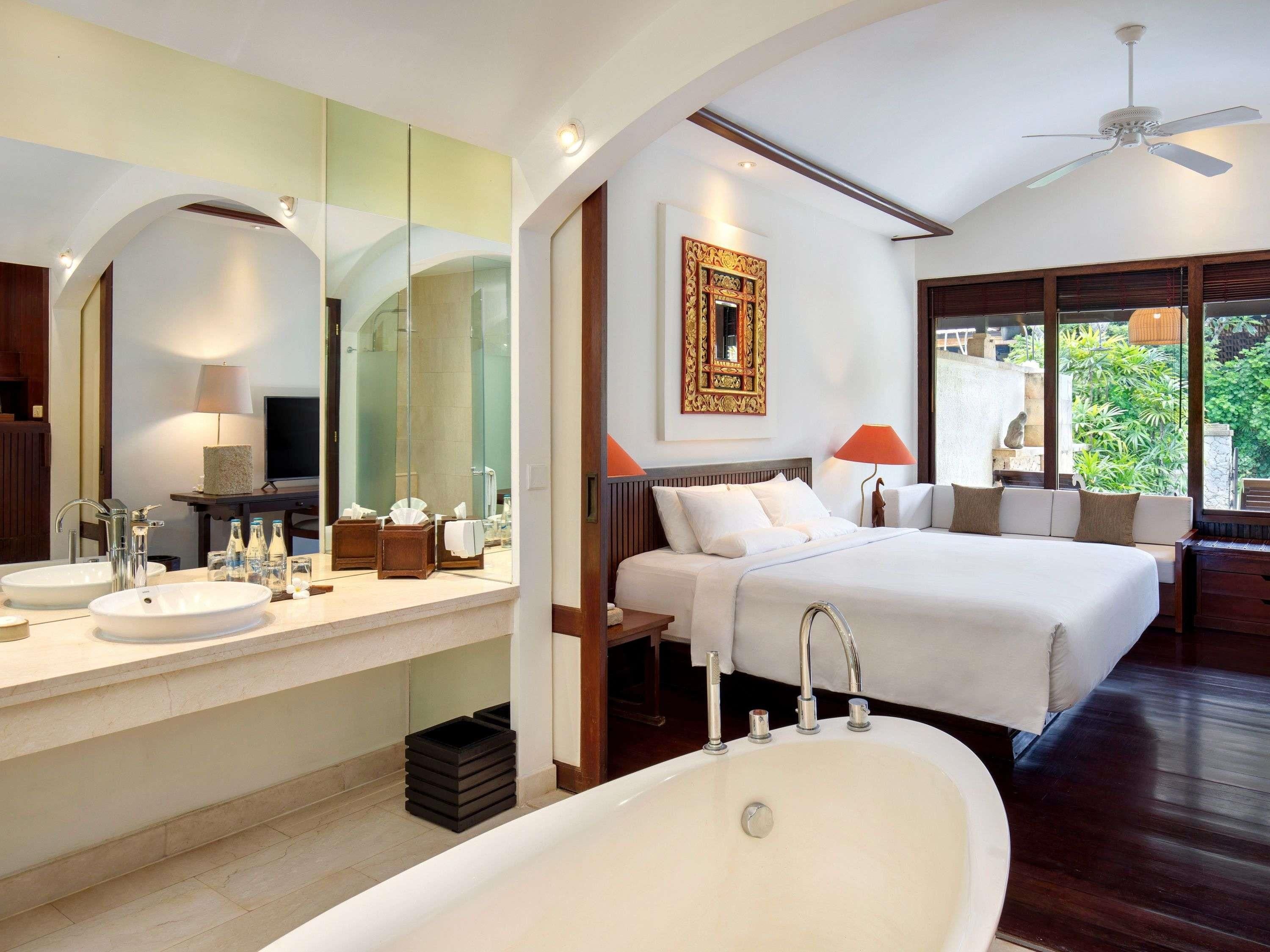 Una habitación de hotel moderna con una cama grande, dos lavamanos, una bañera y un espejo amplio.