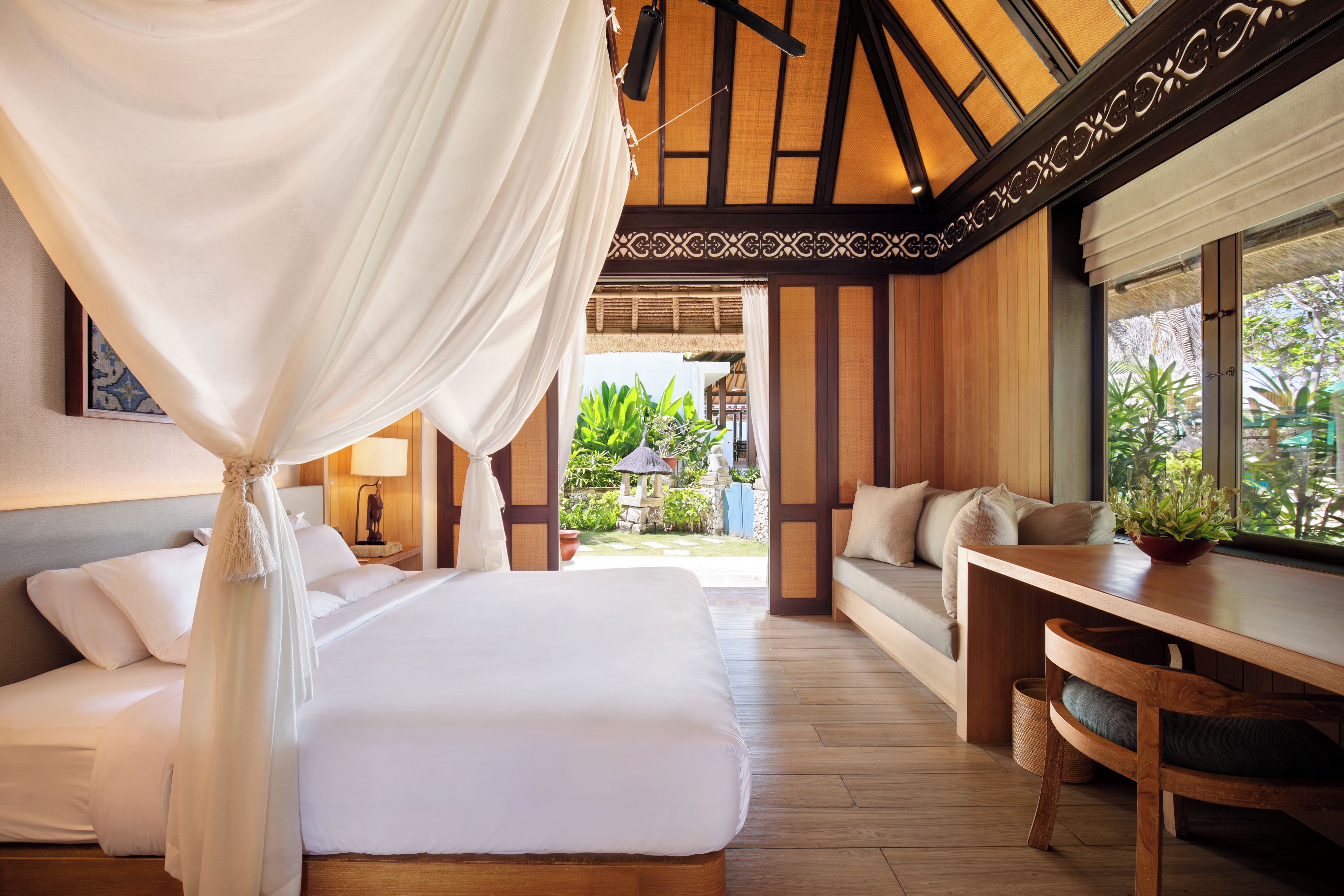 A bedroom with a canopy bed, a sitting area with a table and chairs, and a view of the garden.