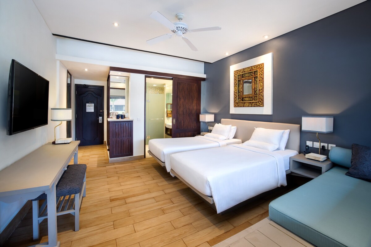 A hotel room with two beds, a desk, a TV, and a ceiling fan.