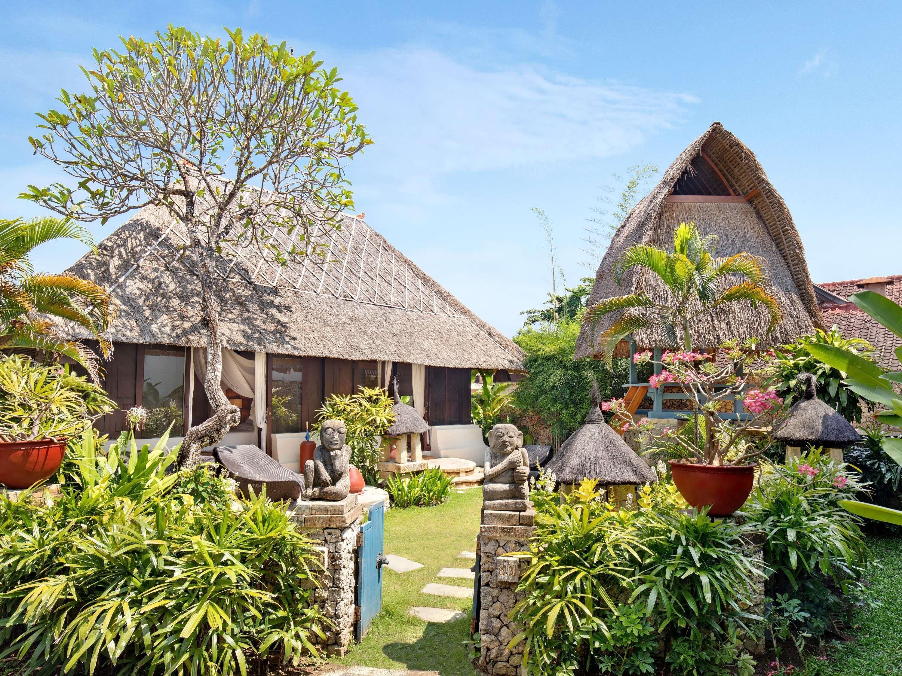 Un complexe hôtelier tropical doté de bâtiments aux toits de chaume, d’une végétation luxuriante et de sentiers pavés de pierres.