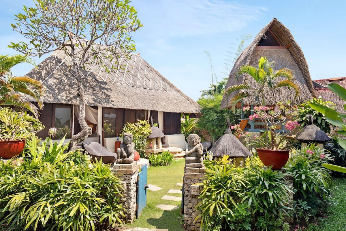 Un complexe hôtelier tropical doté de bâtiments aux toits de chaume, d’une végétation luxuriante et de sentiers pavés de pierres.