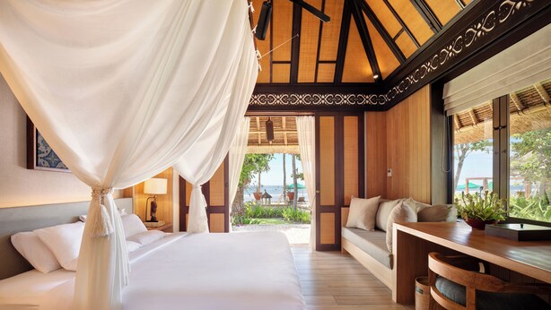 A bedroom with a canopy bed, wooden flooring, a sofa, and a view of the outdoors. - Novotel Bali Benoa (Nusa Dua)