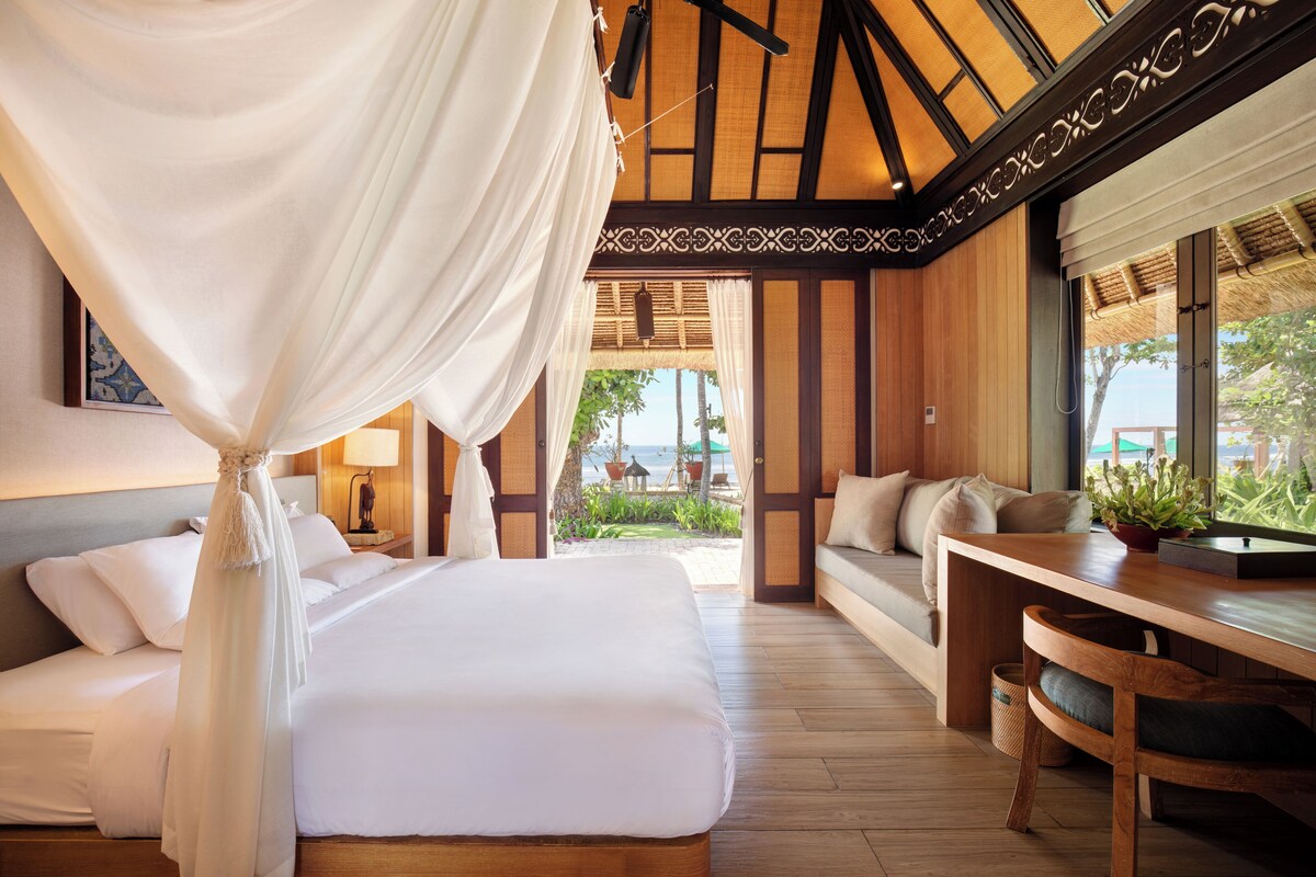 A bedroom with a canopy bed, wooden flooring, a sofa, and a view of the outdoors.