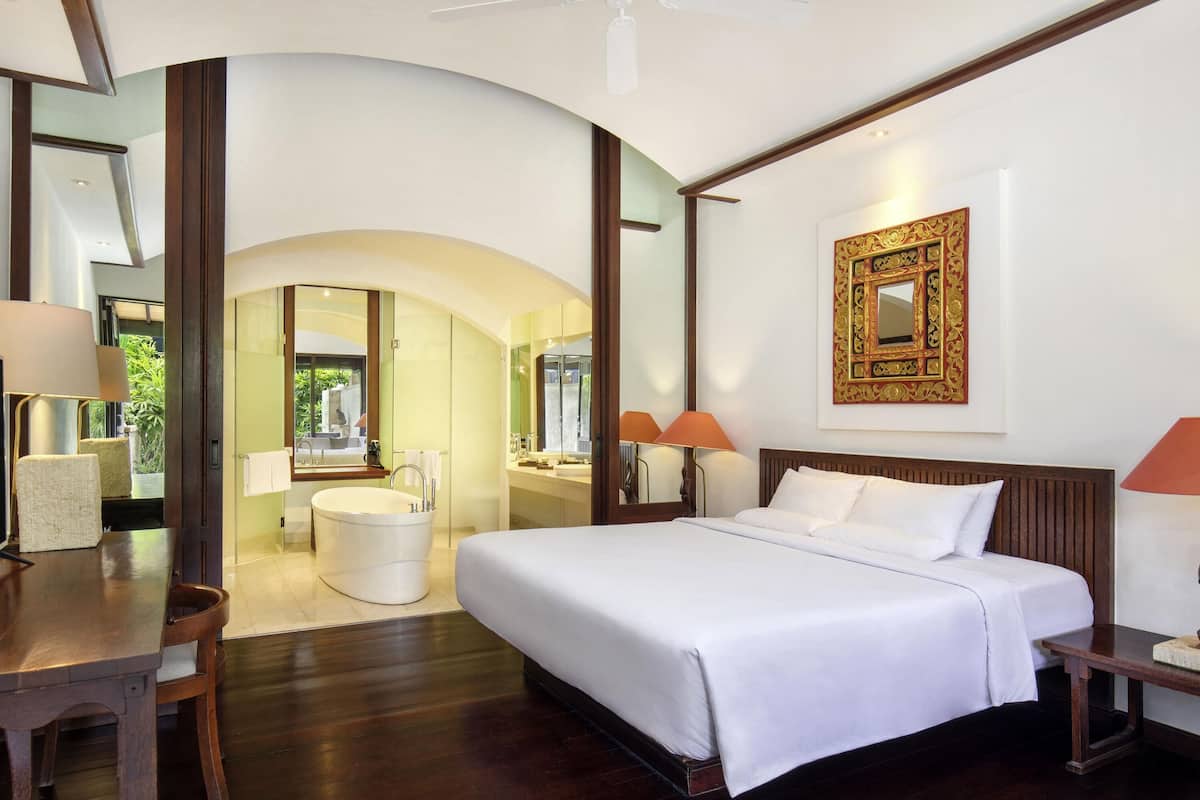 Une chambre d’hôtel avec un grand lit, un bureau, une coiffeuse avec un miroir et une baignoire.