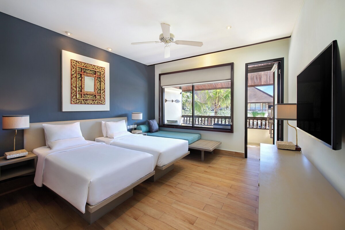A hotel room with two beds, a ceiling fan, a large window with a view, and a flat-screen TV.