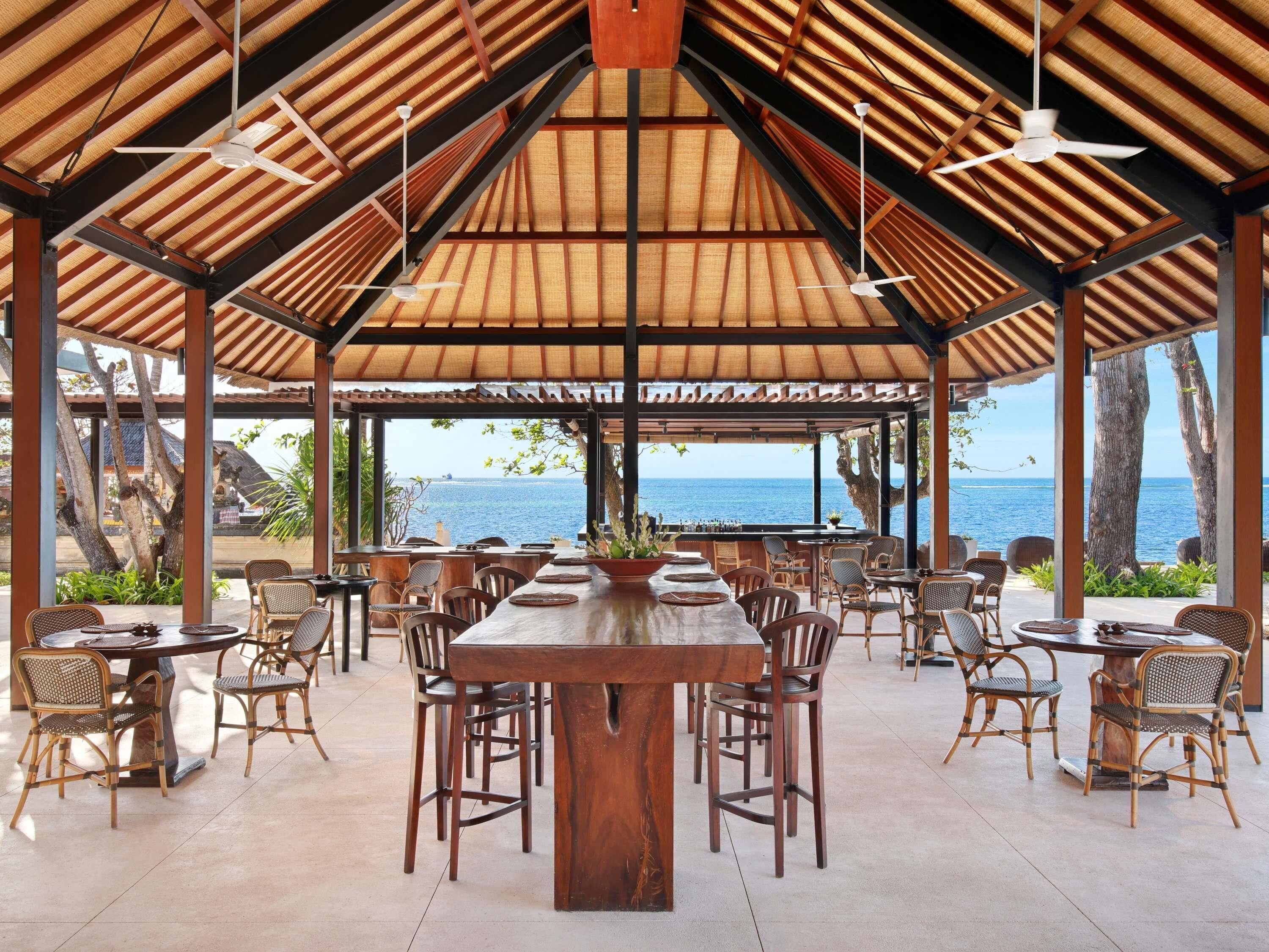 Un área de comedor al aire libre cubierta con una mesa larga y sillas, una barra y vistas al mar.
