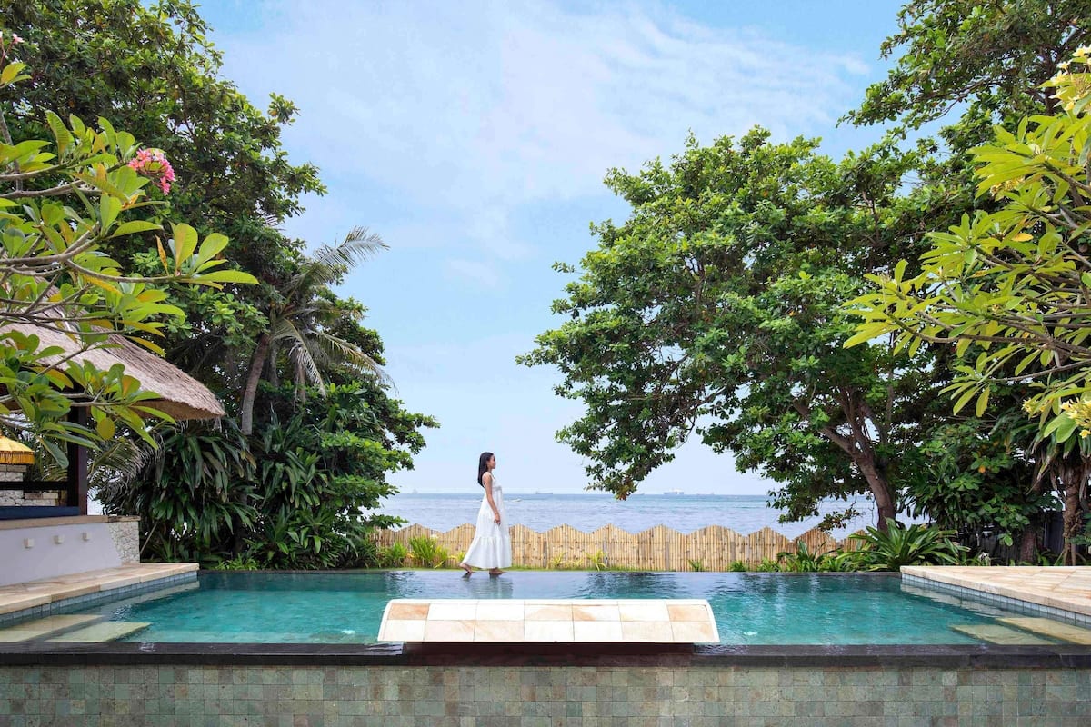 Une piscine avec vue sur la mer, entourée d’une végétation luxuriante et d’une clôture en bois.