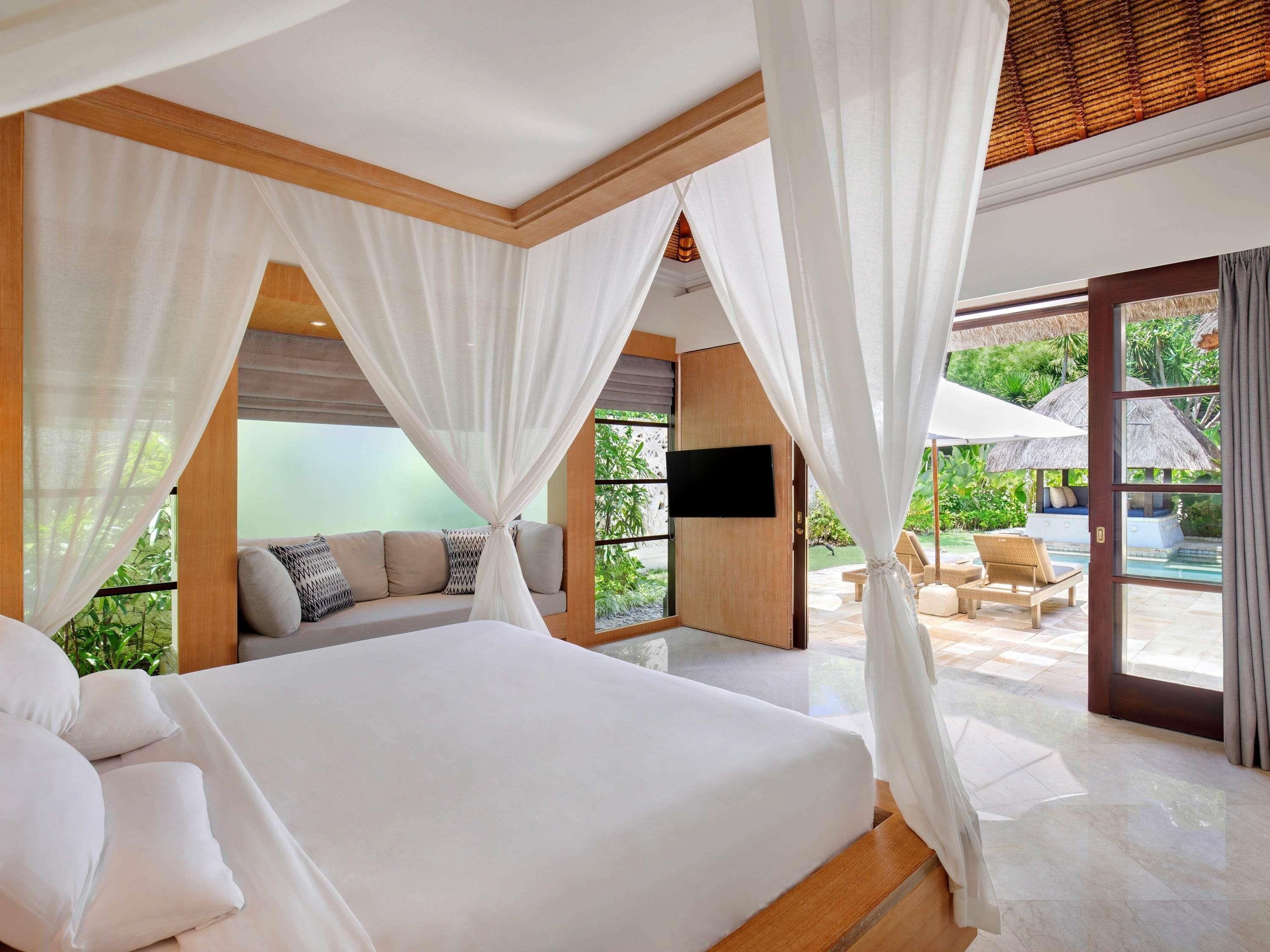 Ein geräumiges Schlafzimmer mit einem großen Bett, einem Fernseher und Blick auf einen Pool sowie eine Sitzgelegenheit im Freien.