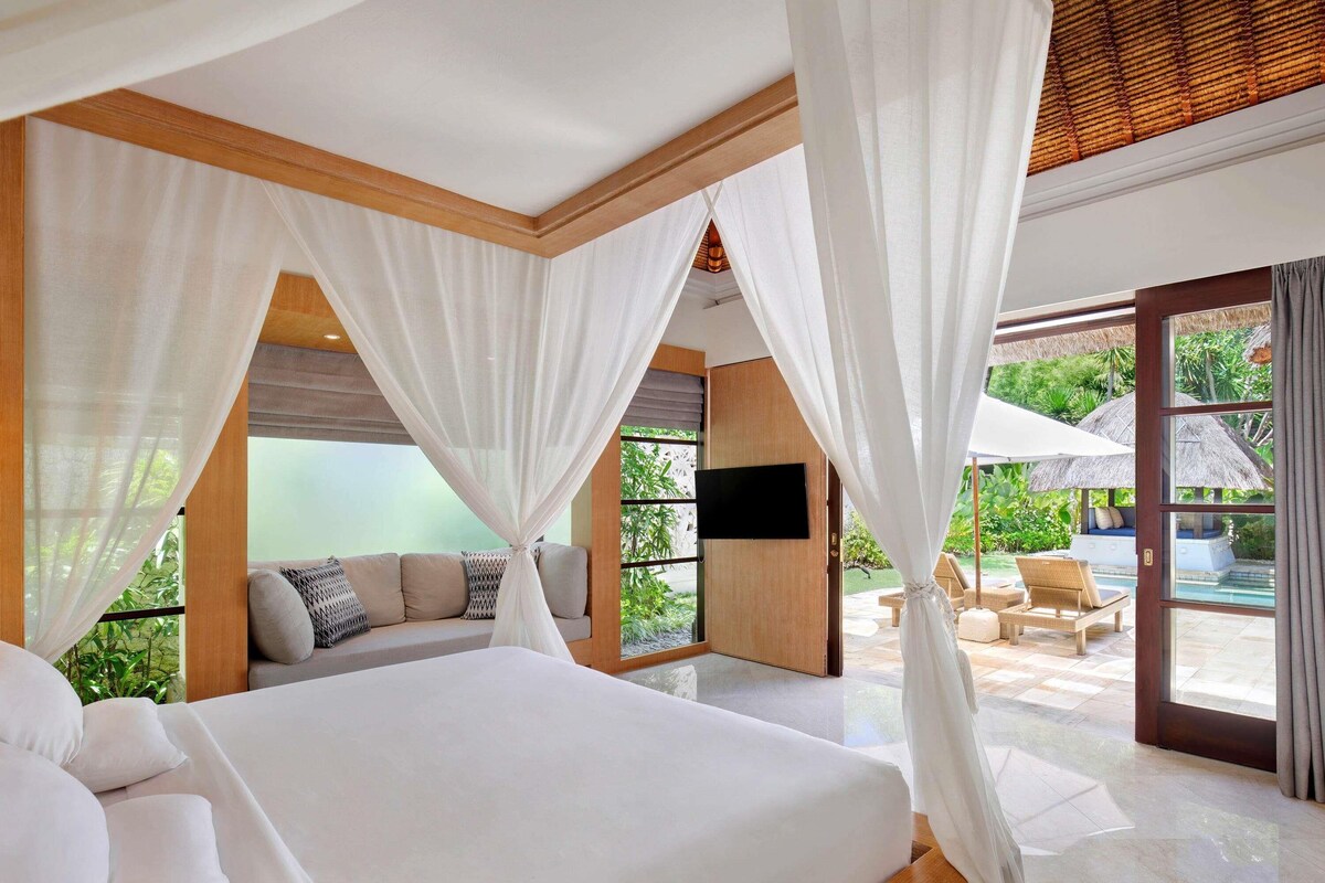 A spacious bedroom with a large bed, a TV, and a view of a pool and outdoor seating area.