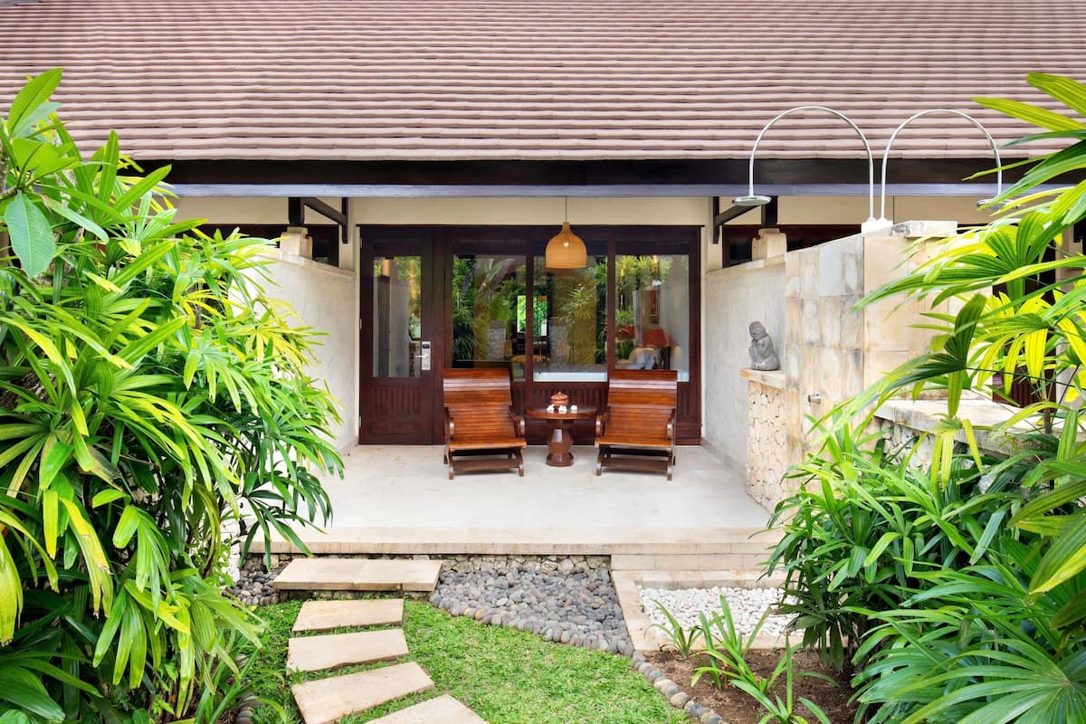 A modern house with a tiled roof, a wooden bench outside, and lush greenery.
