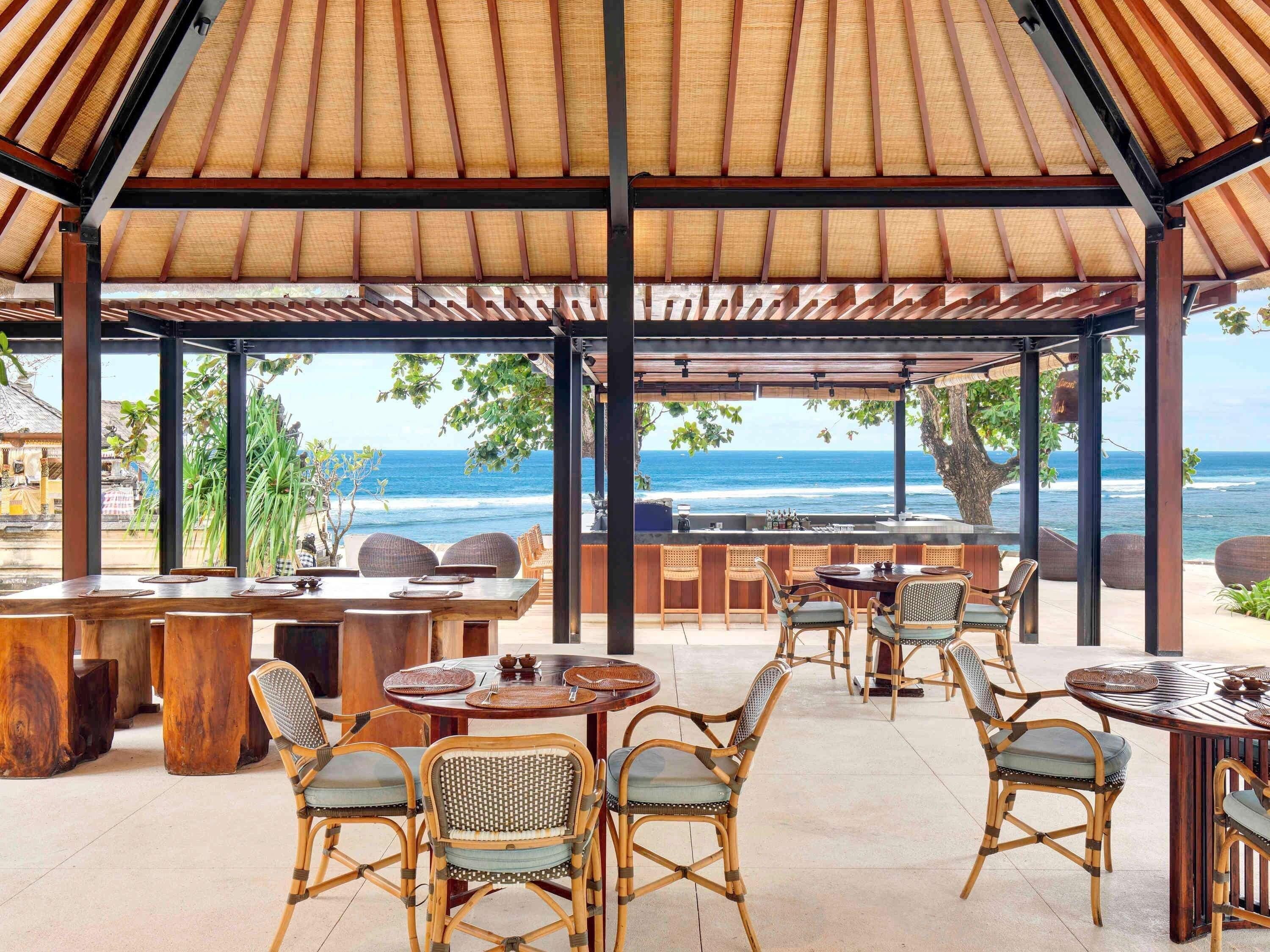 A covered outdoor seating area with tables and chairs, overlooking the ocean.